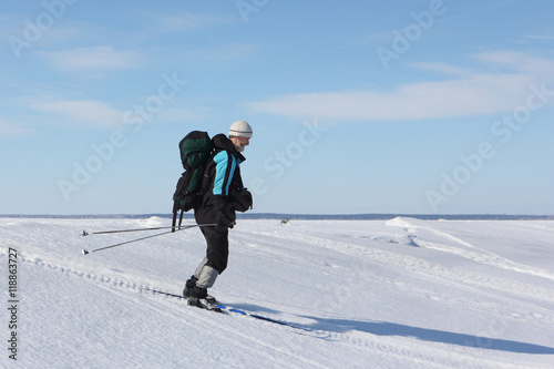 The man the traveler with a backpack skiing on snow of the frozen river
