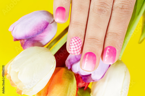 Hand with manicured nails covered with pink nail polish and tulip flowers