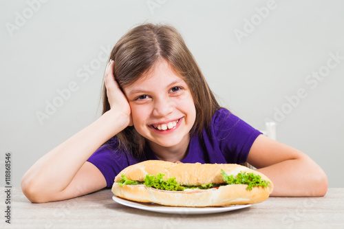 Little girl is happy because she likes to eat sandwich for breakfast.