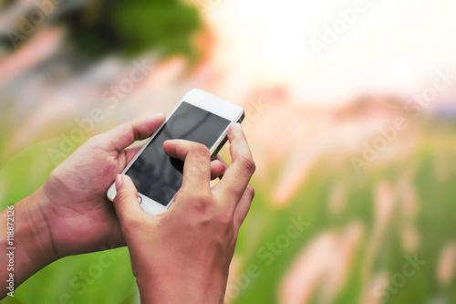 Hand hold and touch screen smart phone, on natural green blurred background.