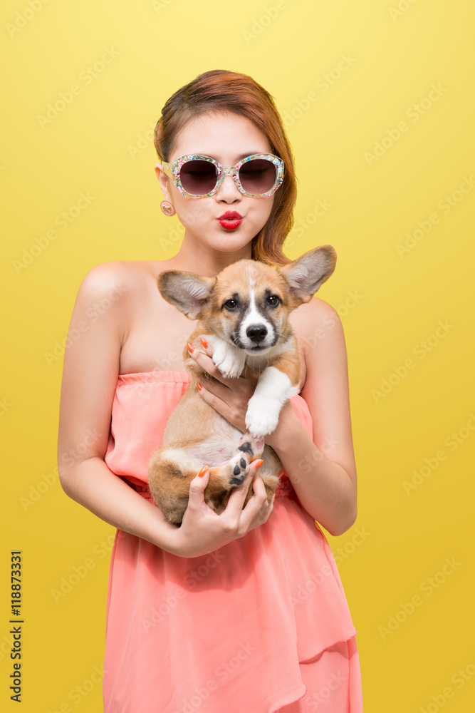 Beautiful young asian woman in nice spring dress, posing in studio with corgi puppy. Fashion photo.