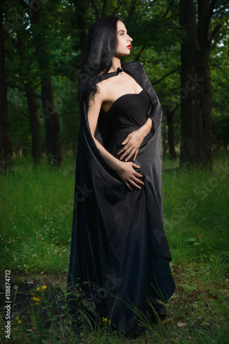 Beautiful brunette woman in black dress and black cloak in the m