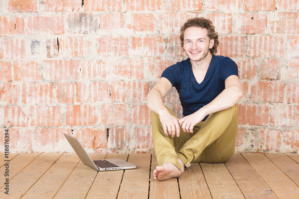 Happy man with a laptop in front of a brick wall. Handsome man working in room. Modern lifestyle