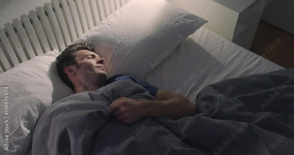 Dreaming man tosses and turns, restless as he sleeps in a double bed
