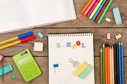 inscription of "school", book, calculator, notepad and other stationery on brown wooden table