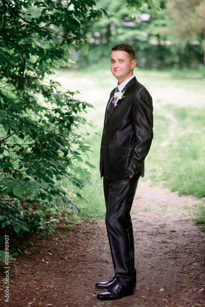 Attractive groom in black suit and black shoes stands on the pat