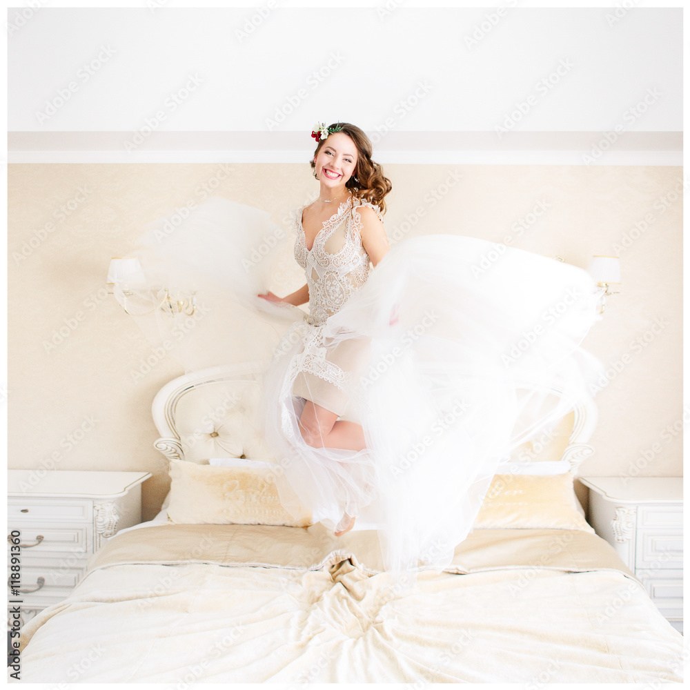 Happy bride with dark blonde hair jumps on the bed Happy bride with dark blonde hair jumps on the bed