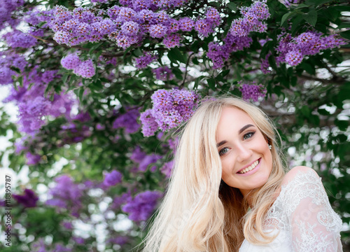 Violet flowers of lilac hang over the smiling blonde lady