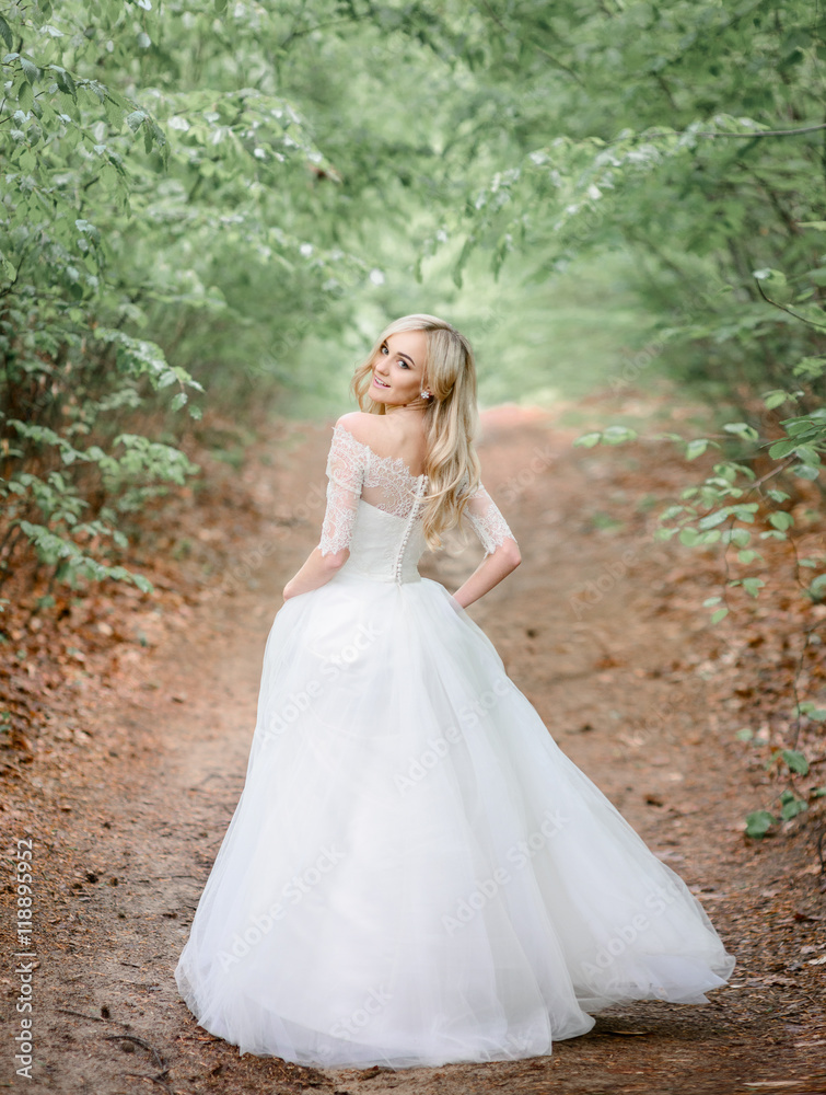 Sweet blonde bride looks over her shoulder while walking along t Sweet blonde bride looks over her shoulder while walking along t