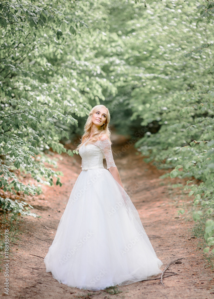 Green branches hang over the path where beautiful bride stands
