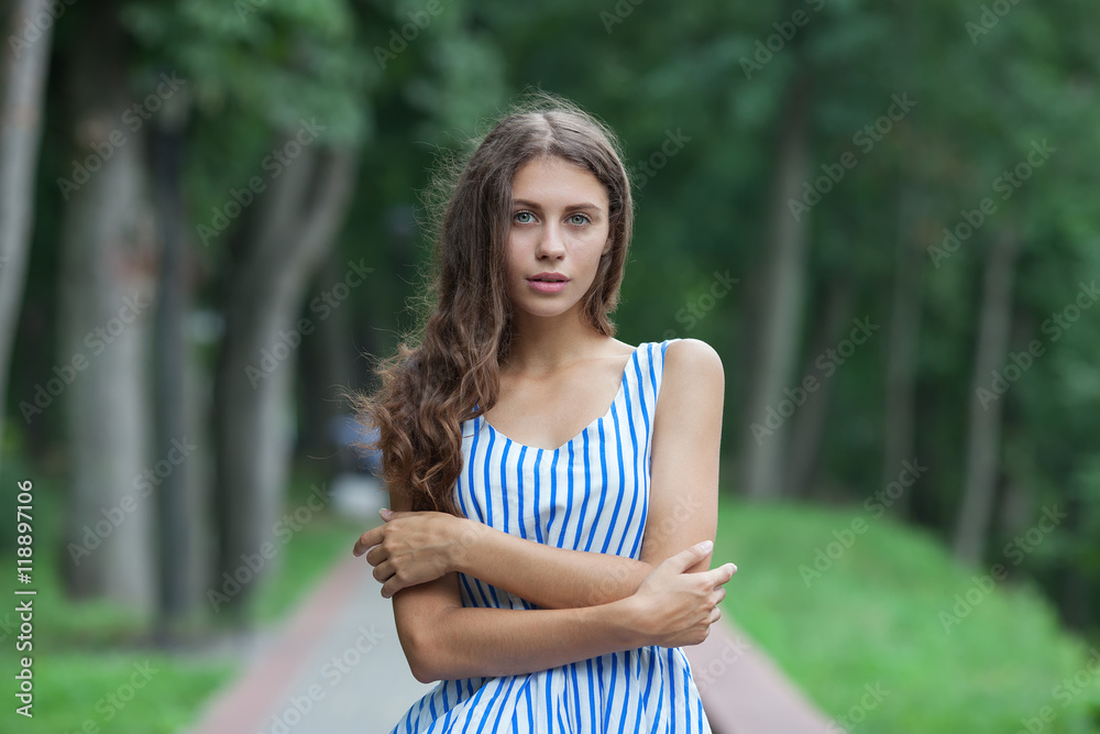 Spring beautiful woman in summer dress walking in green park enjoying weekend. Playful and beautiful caucasian girl on warm sunny day.