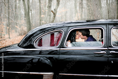 Groom in dark blue jacket leans to bride for a kiss while sittin
