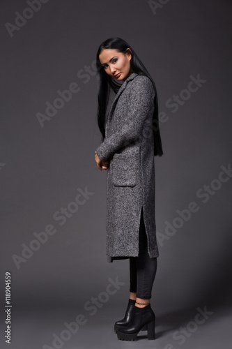 Picture of beautiful brunette model woman smiling for camera while promoting expensve clothes isolated on grey background in studio.