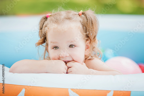 The little baby girl playing with toys in inflatable pool in the summer sunny day