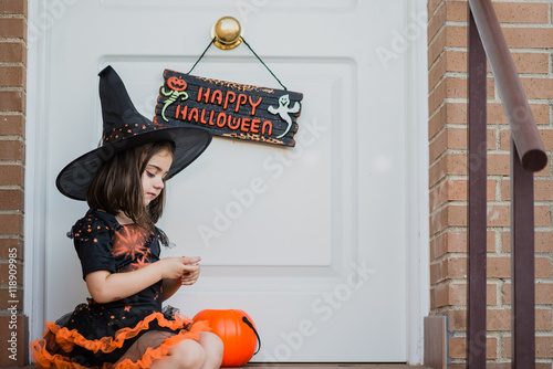 Cute little witch looking at her hands in front of door