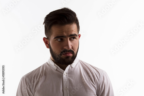 Picture of thoughtful handsome hipster man looking away while posing in studio. Bearded brunette man posing isolated on white background. Hard light concept.