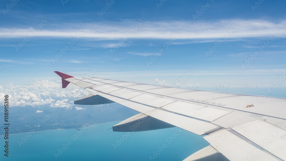 Fototapeta premium Wing of a plane from window view with bright blue sky and sea background.