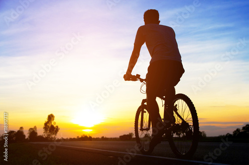 silhouette men cycling on road at sunset