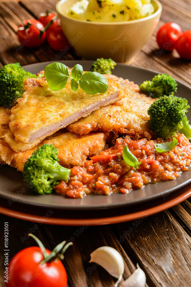 Piccata - fried pork cutlets stuffed with smoked ham slices coated in cheese and eggs served with tomato sauce, steamed broccoli and boiled potatoes Piccata - fried pork cutlets stuffed with smoked ham slices coated in cheese and eggs served with tomato sauce, steamed broccoli and boiled potatoes
