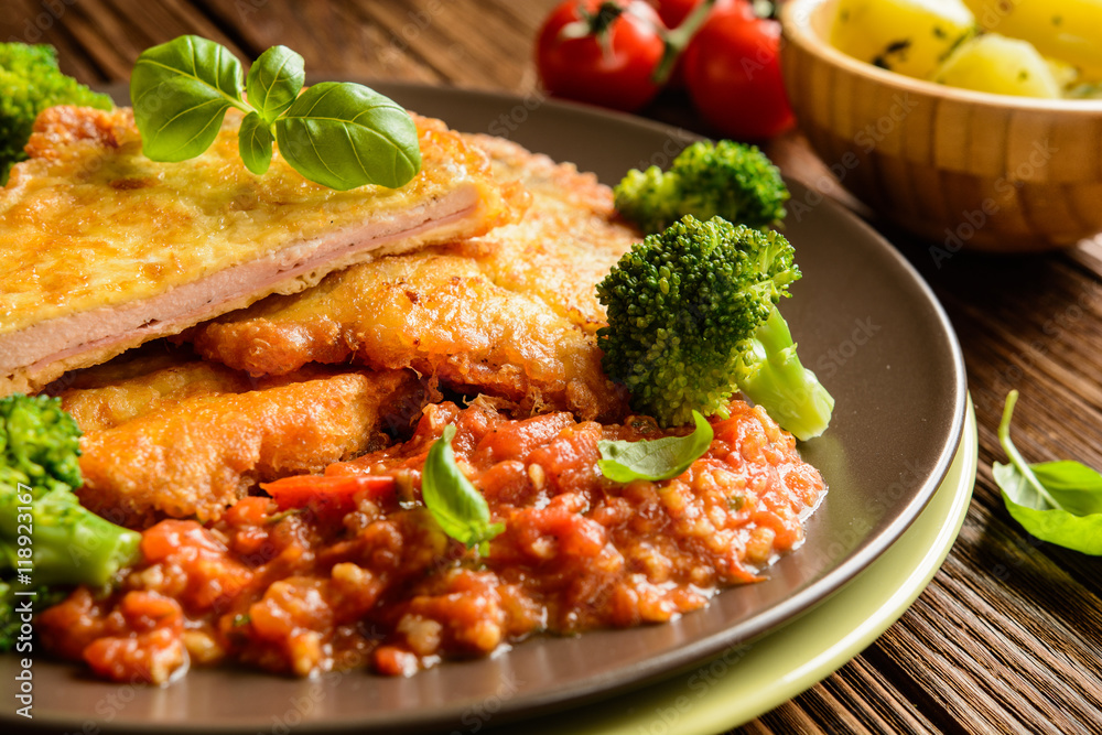 Piccata - fried pork cutlets stuffed with smoked ham slices coated in cheese and eggs served with tomato sauce, steamed broccoli and boiled potatoes Piccata - fried pork cutlets stuffed with smoked ham slices coated in cheese and eggs served with tomato sauce, steamed broccoli and boiled potatoes