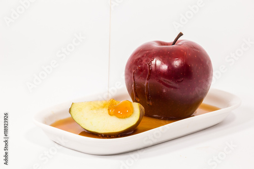 Pouring honey on red apple and red apple slice on white plate with honey isolated on a white background