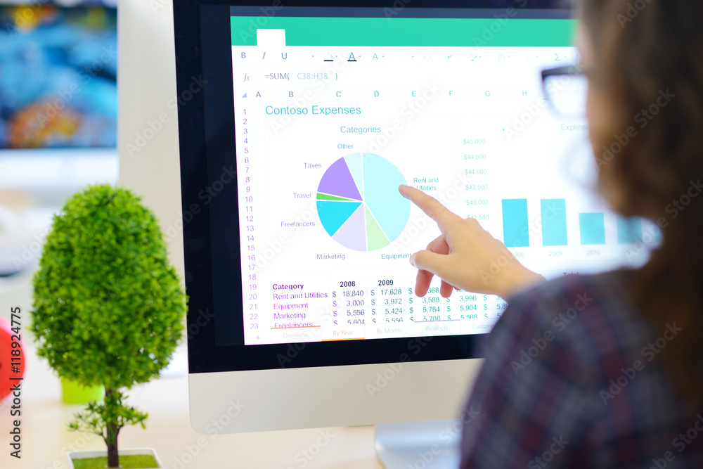 Over the shoulder view of a businesswoman working at computer and pointing to graph on screen Over the shoulder view of a businesswoman working at computer and pointing to graph on screen