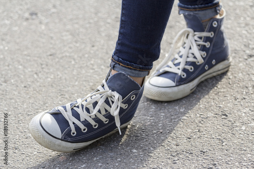 Women's feet in sneakers are standing on the sidewalk