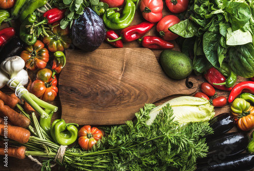 Fresh raw vegetable ingredients for healthy cooking or salad making with rustic wood board in center, top view, copy space, horizontal composition. Diet or vegetarian food concept photo
