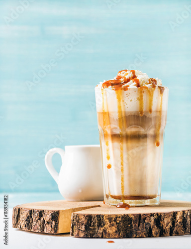 Photos Latte macchiato with whipped cream and caramel sauce in tall glass on wooden boa