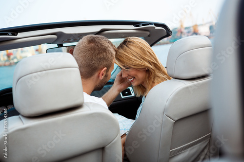 Young beautiful couple smiling, sitting in car near sea.