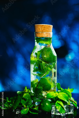 mojito bottle with lime and mint ice cube close-up on blue background