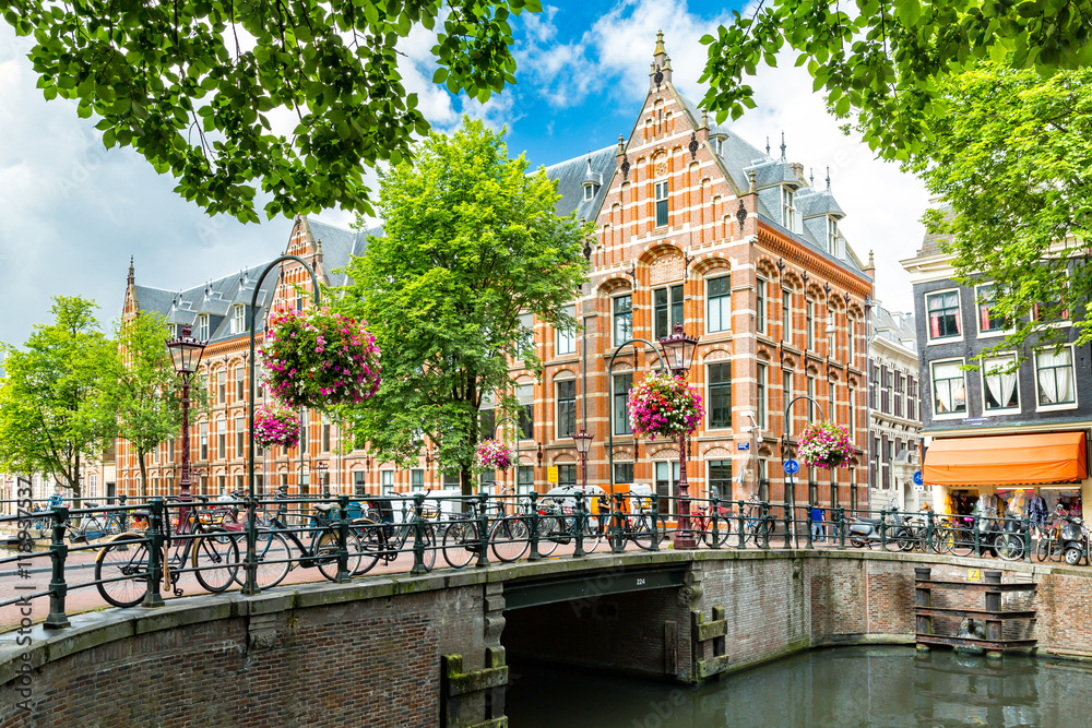 Fototapeta premium Typowy pejzaż miejski Amsterdamu od strony kanału, naprzeciwko XVII-wiecznej siedziby holenderskiej Kompanii Wschodnioindyjskiej, obecnie używany przez Uniwersytet w Amsterdamie