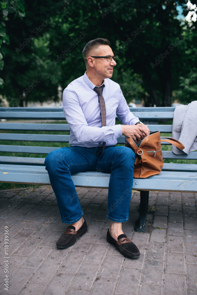 Image of business man open his bag while sitting on the park bench outdoor Image of business man open his bag while sitting on the park bench outdoor