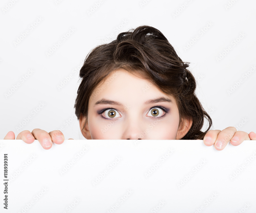Smiling happy young woman standing behind and leaning on a white blank billboard or placard, expresses different Smiling happy young woman standing behind and leaning on a white blank billboard or placard, expresses different