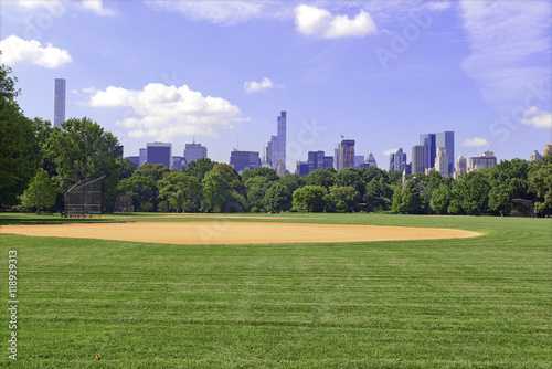 Green grass and baseball field of Central Park with Manhattan skyline and blue sky