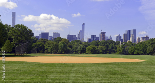 Green grass and baseball field of Central Park with Manhattan skyline and blue sky