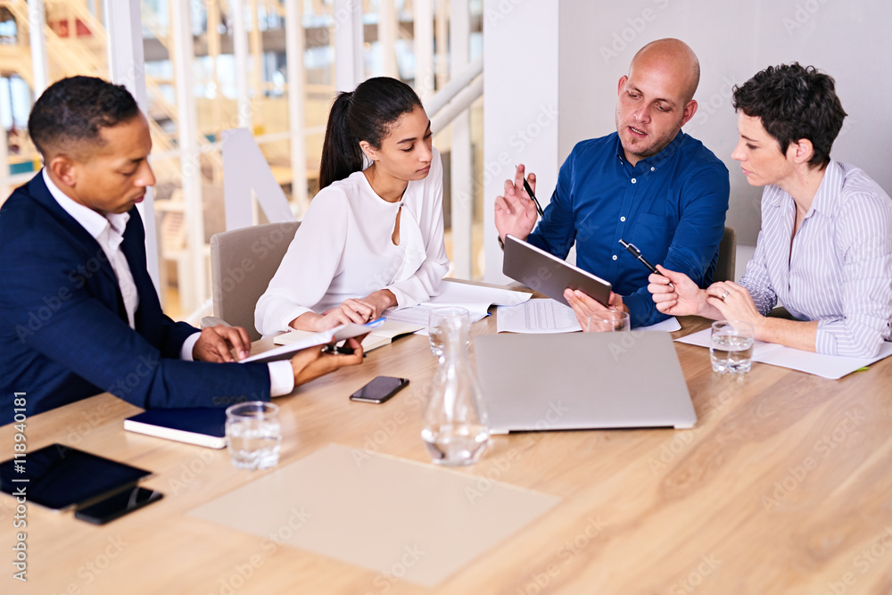 Fototapeta premium Business meeting taking place with diverse group of business people in a modern office with several electronic devices at their aid, including the tablet being held by one of the executives.