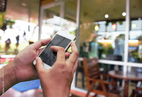 Hand hold and touch screen smart phone, on abstract blur coffee shop for background .