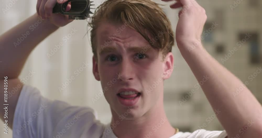Handsome young man brushing his hair and singing to himself in a bathroom with shower curtain behind.  Slow motion recorded at 60fps, close up, front view from mirror POV.