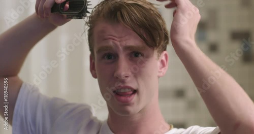 Handsome young man brushing his hair and singing to himself in a bathroom with shower curtain behind.  Slow motion recorded at 60fps, close up, front view from mirror POV.