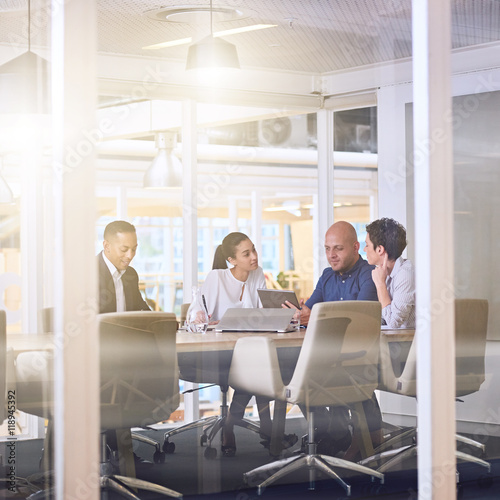 Corporate business meeting in modern office with glass walls, flare from the sunlight and reflections on the glass while business discussions take place amongst board members.