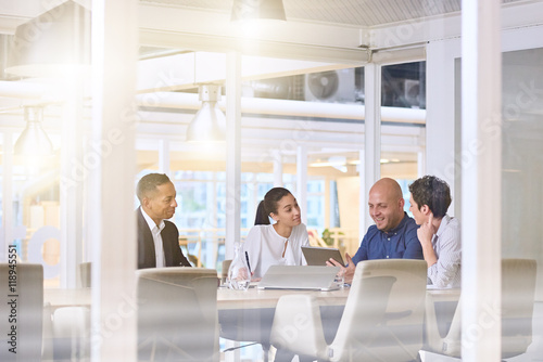 Corporate business meeting in modern office with glass walls, flare from the sunlight and reflections on the glass while business discussions take place amongst board members.