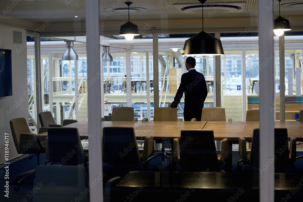 Successful business man with ambition standing alone in conference room while looking out the window thinking about several business stratergies that he might have to pursue soon. Successful business man with ambition standing alone in conference room while looking out the window thinking about several business stratergies that he might have to pursue soon.