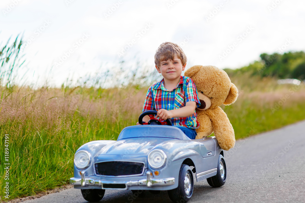 Little kid boy driving big toy car with a bear, outdoors. Little kid boy driving big toy car with a bear, outdoors.