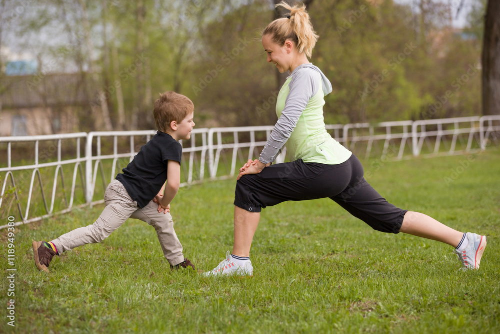 Obraz premium Happy son and mother are doing exercises in the summer park. on the stadium, outdoor. Sport activities with children. Healthy lifestyle. Fitness exercises. Young mother and son are stretching together