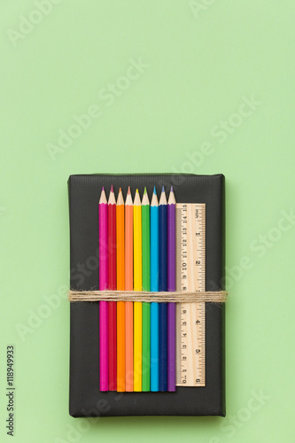 Colorful school and office supplies - pencils and ruler on black book and light green background. Top view with copy space.