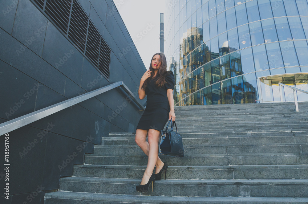 business girl in a dress walks down the stairs holding a bag