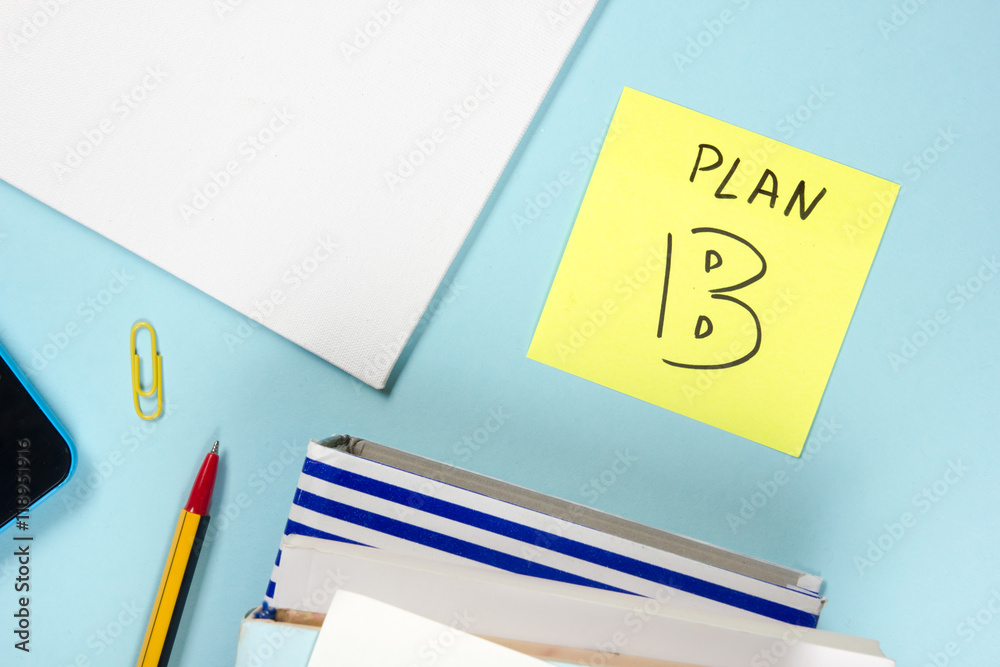 Plan B.Office table desk with supplies, blank note pad, cup, pen, pc, crumpled paper, flower on blue background. Top view Plan B.Office table desk with supplies, blank note pad, cup, pen, pc, crumpled paper, flower on blue background. Top view