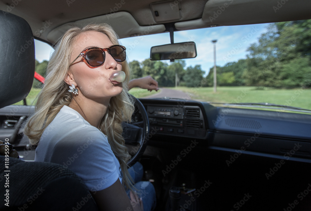 Naklejka premium Junge Frau am Steuer eines Autos kaut Kaugummi und macht eine Blase
