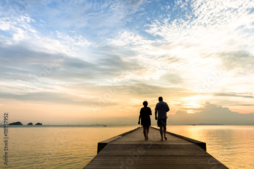 Couple walks along the pier at sunset over the sea 